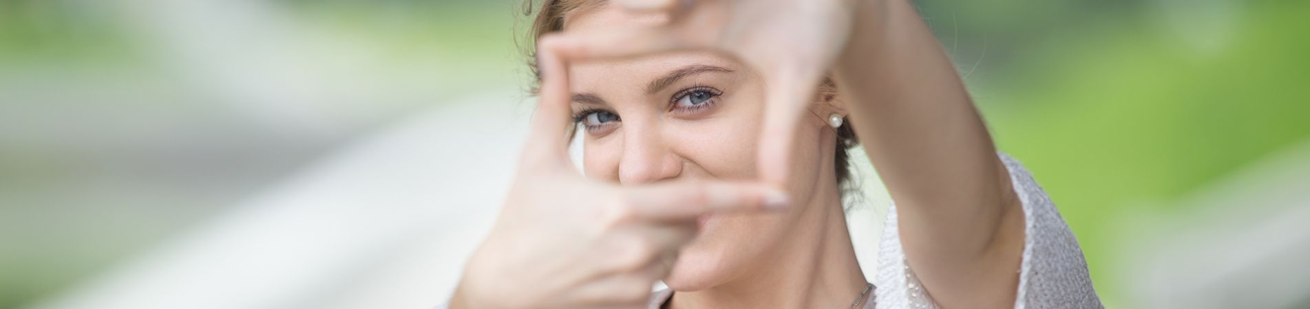 Frau bildet mit den Fingern einen Rahmen und blickt lächelnd hindurch