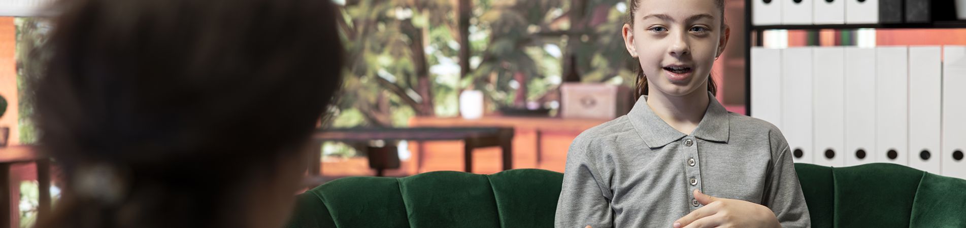 Mädchen sitzt auf einem Sofa und spricht mit einer Erwachsenen