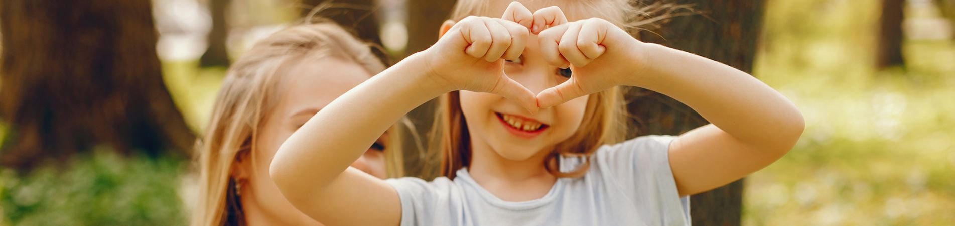 Ein Mädchen ist mit ihrer Mutter im Wald und bildet mit den Fingern ein Herz