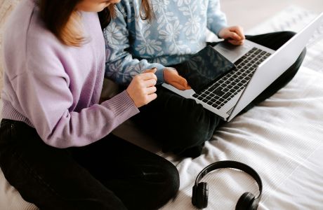 Zwei Mädchen sitzen auf dem Bett und schauen auf einen Laptop